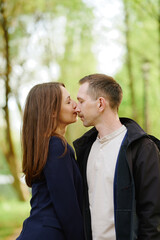 Naklejka premium romantic couple sharing gentle kiss outdoors, surrounded by lush greenery. woman in blue, man in jacket, expressing love and connection. captures essence of intimacy in nature