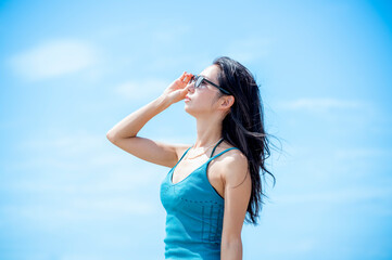 Young woman in a ribbed blue dress standing confidently at the seaside with hands raised and...