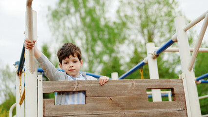 boy enjoying playground adventure on wooden structure. child holding onto railing, experiencing...