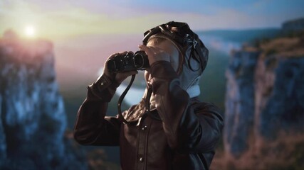 Curious young adventurer dressed as a pilot scans the horizon with binoculars against a dramatic natural backdrop. - Powered by Adobe