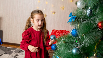 Little girl wearing red christmas dress and to decorate Christmas Tree at home