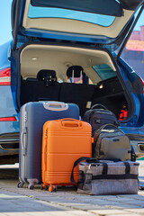 Suitcases and bags in front of open car trunk, standing on pavement near suburban house. Luggage...