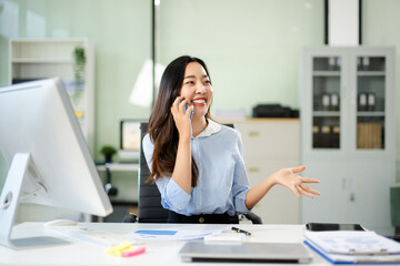 Asian businesswoman chatting on mobile at her desk. Bright office vibe, communication, productivity, success