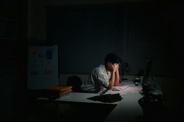 Tired male employee sits in a dark office, working overtime under dim lighting © Prathankarnpap