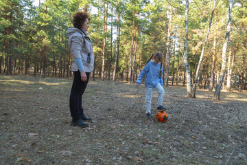 Grandmother and granddaughter playing with a ball in the forest in sunny day.