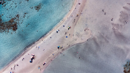 Aerial drone views of Elafonissi Beach reveal its stunning pink sand, turquoise waters, and shallow...