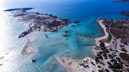 Aerial drone views of Elafonissi Beach reveal its stunning pink sand, turquoise waters, and shallow...