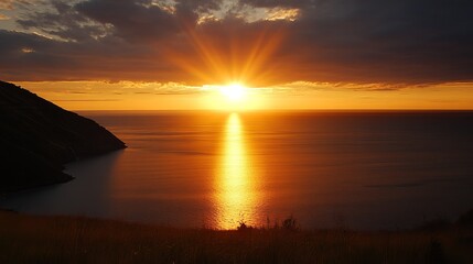 Fototapeta premium A breathtaking sunset over a calm ocean, the sun's rays casting a golden path across the water, silhouetting a coastal landscape