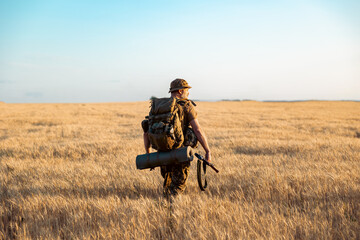 military man with a backpack in the field. Soldier goes on a mission.