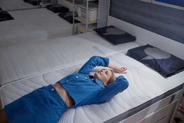 Woman relaxes on a modern mattress in a stylish showroom store, showcasing ultimate comfort