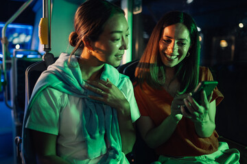 Two young women using a smartphone and riding bus at night