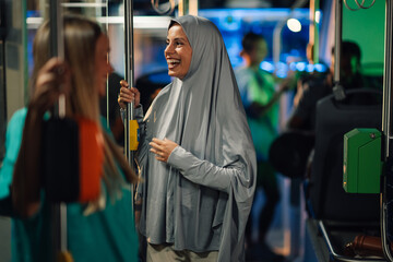 Muslim woman wearing hijab smiling and talking on the bus with her friend