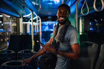 Smiling sporty man using smartphone on a night bus ride home