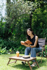 Young woman reading a book and relaxing in a lush green garden