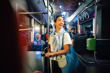 Young woman standing on a bus at night holding smartphone and luggage