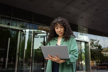 Focused woman using laptop outside modern building