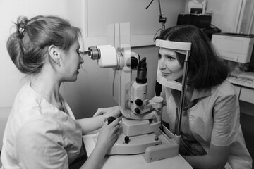 Female doctor examines young womans eye using professional vision testing equipment in clinic
