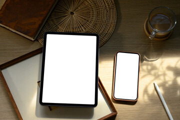 Tablet and smartphone with blank screens on wooden desk surrounded by books and coffee cup