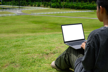 Woman working on laptop with blank screen outdoors in a green park. Technology lifestyle concepts