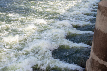 Rapidly flowing water with large waves over a dam on a river, water flow at the dam gate