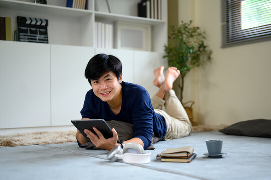 Happy man lying on carpet and using digital tablet in cozy living space