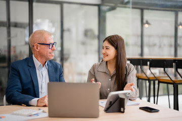 Businesspeople discussing and working using laptop and tablet in modern office, senior businessman and young businesswoman talking and working together