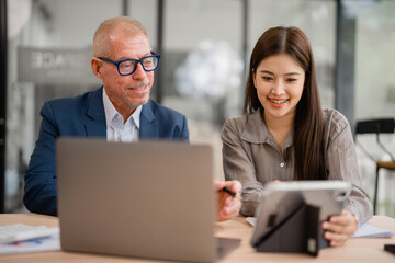 Senior businessman and young businesswoman discussing and working together using laptop and tablet...