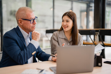 Two business professionals engaging in a work discussion while collaborating on a laptop in a...