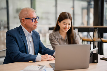 Senior caucasian manager and young asian businesswoman are using laptop and digital tablet, working...