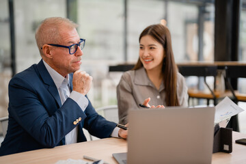 Senior businessman listening to young businesswoman explaining project during meeting in modern...