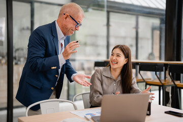 Senior manager coaching a young asian businesswoman using laptop in a modern office, they're...