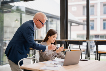 Senior manager coaching young asian businesswoman and explaining new project using laptop and...