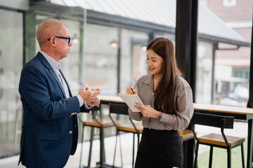 Senior Caucasian manager engaging with a young Asian businesswoman, explaining work concepts while...