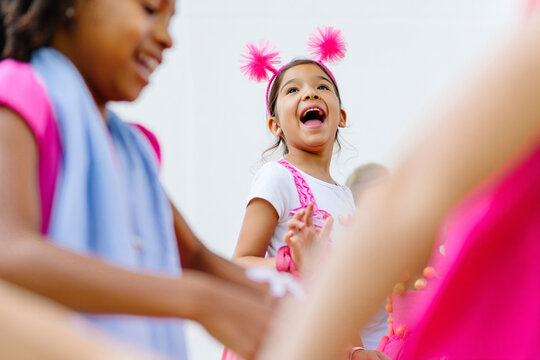 Joyful little girl in a pink headband laughs and claps, celebrating or playing. Candid close-up portrait capturing happy childhood moments with vibrant energy.