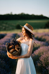 Woman in white dress holds basket of bread and lavender in blooming field at sunset