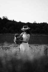 Woman in hat gathers flowers in a field during sunset near a forested area