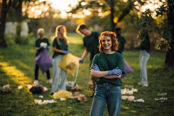 Young woman volunteer smiling with arms crossed picking up trash in park