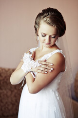 A woman in a white dress is wearing a lace glove and a veil. She is standing in front of a couch