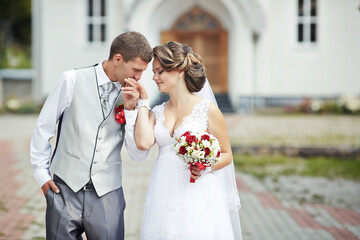 A bride and groom are standing in front of a church, with the bride holding a bouquet
