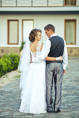 A bride and groom are standing on a stone walkway, posing for a picture. The bride is wearing a...