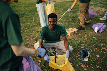Young black man picking up trash with volunteers in a park