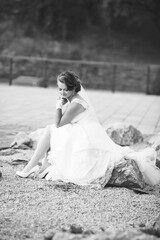 A woman in a white dress sits on a rock. She is wearing a veil and a white dress
