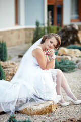 A woman in a white wedding dress sits on a rock. She is wearing a veil and a white dress
