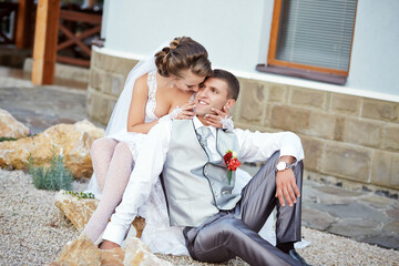 A man and a woman are sitting on a rock, the man is wearing a vest and the woman is wearing a white...