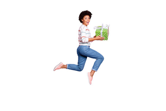 Full length body size photo of excited fast quick crazy funny girlfriend black skinned cute cheerful wearing jeans denim striped sweater holding giftbox with hands isolated pastel color background
