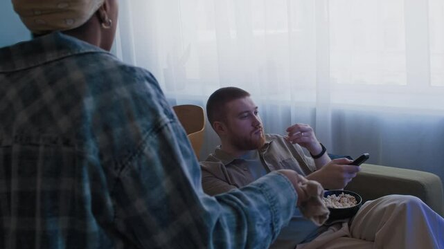 Over shoulder shot of exhausted Black woman scolding her lazy Caucasian husband, holding his dirty socks