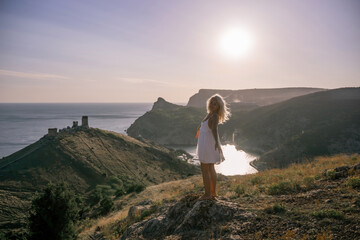 Fototapeta premium A woman stands on a hill overlooking a body of water. The sky is clear and the sun is shining brightly. The woman is enjoying the view and the peaceful atmosphere.