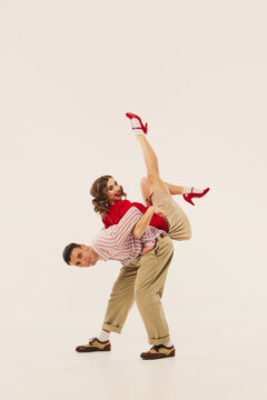 Dancers perform an energetic lindy hop maneuver in retro attire against a plain background. Concept of vintage dance revival and energetic cultural expression.
