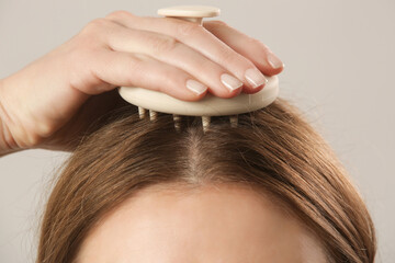 Girl doing herself a head massage using a scalp massager, stimulating hair growth,...