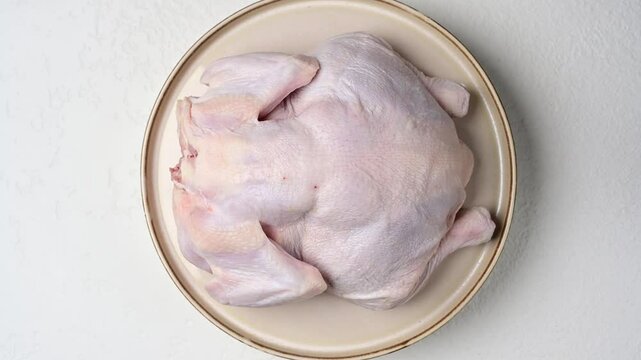 Raw whole chicken on circular plate turns for culinary presentation